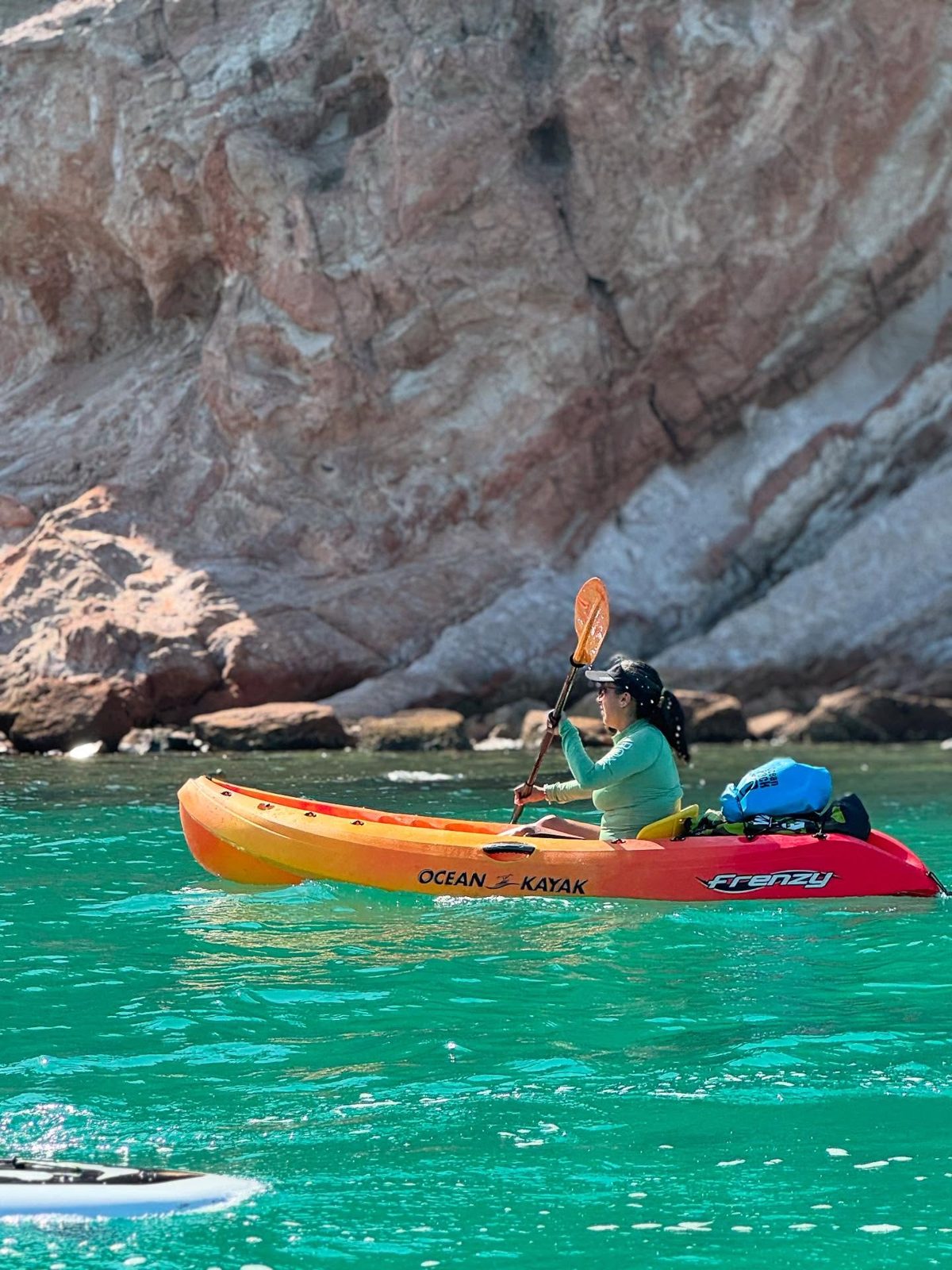 Kayak naranja sobre el agua turquesa junto a un gran acantilado en La Paz