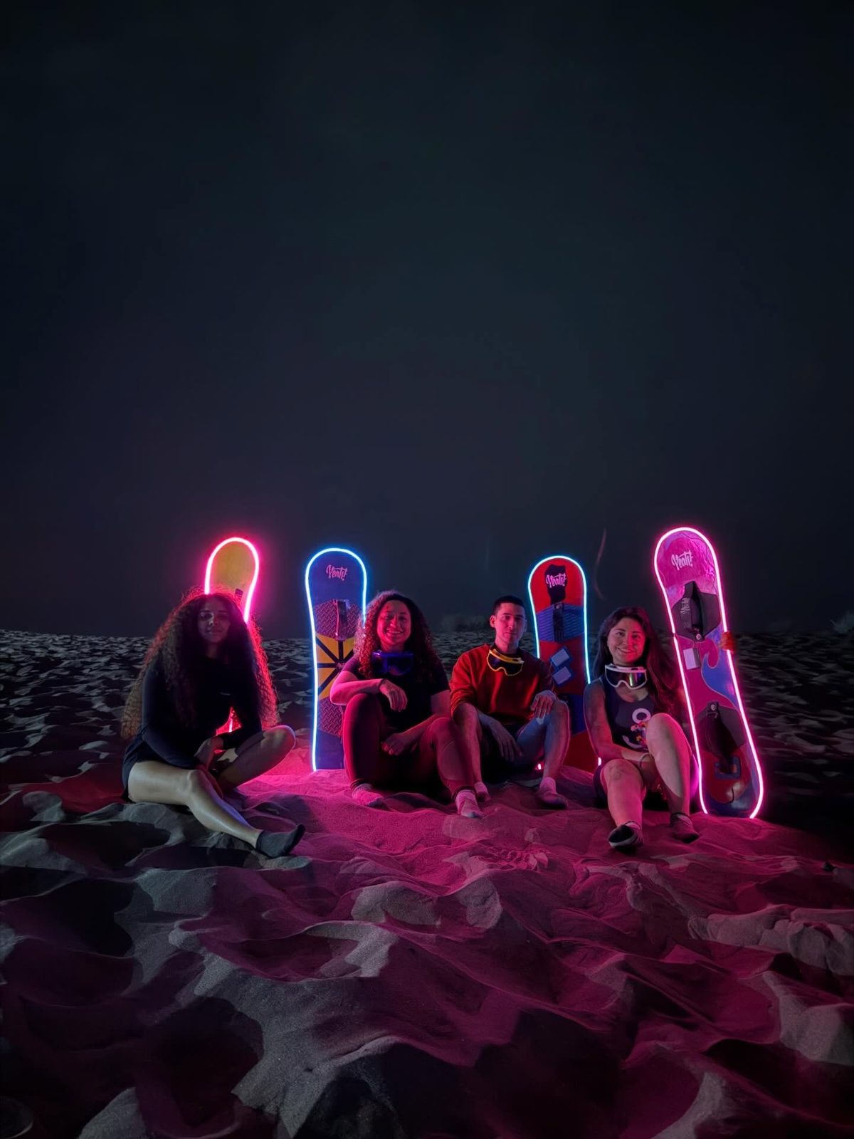 Grupo con tablas de neón encendidas en las dunas durante la sesión nocturna