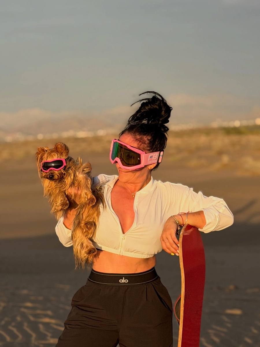 Clienta y su perro, los dos con goggles rosas, en las dunas al atardecer
