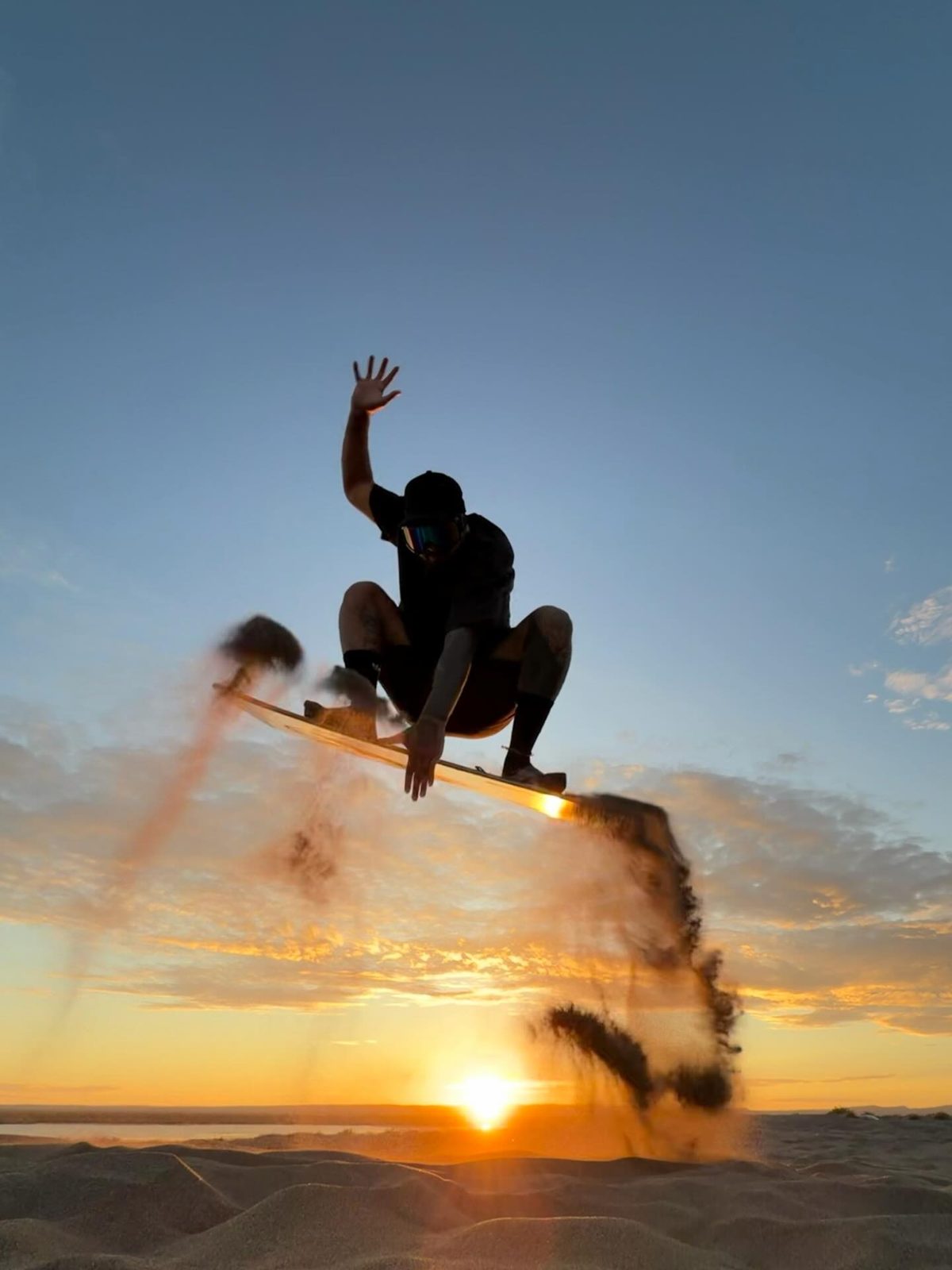 Silueta de un sandboarder saltando frente al sol en las dunas de El Mogote