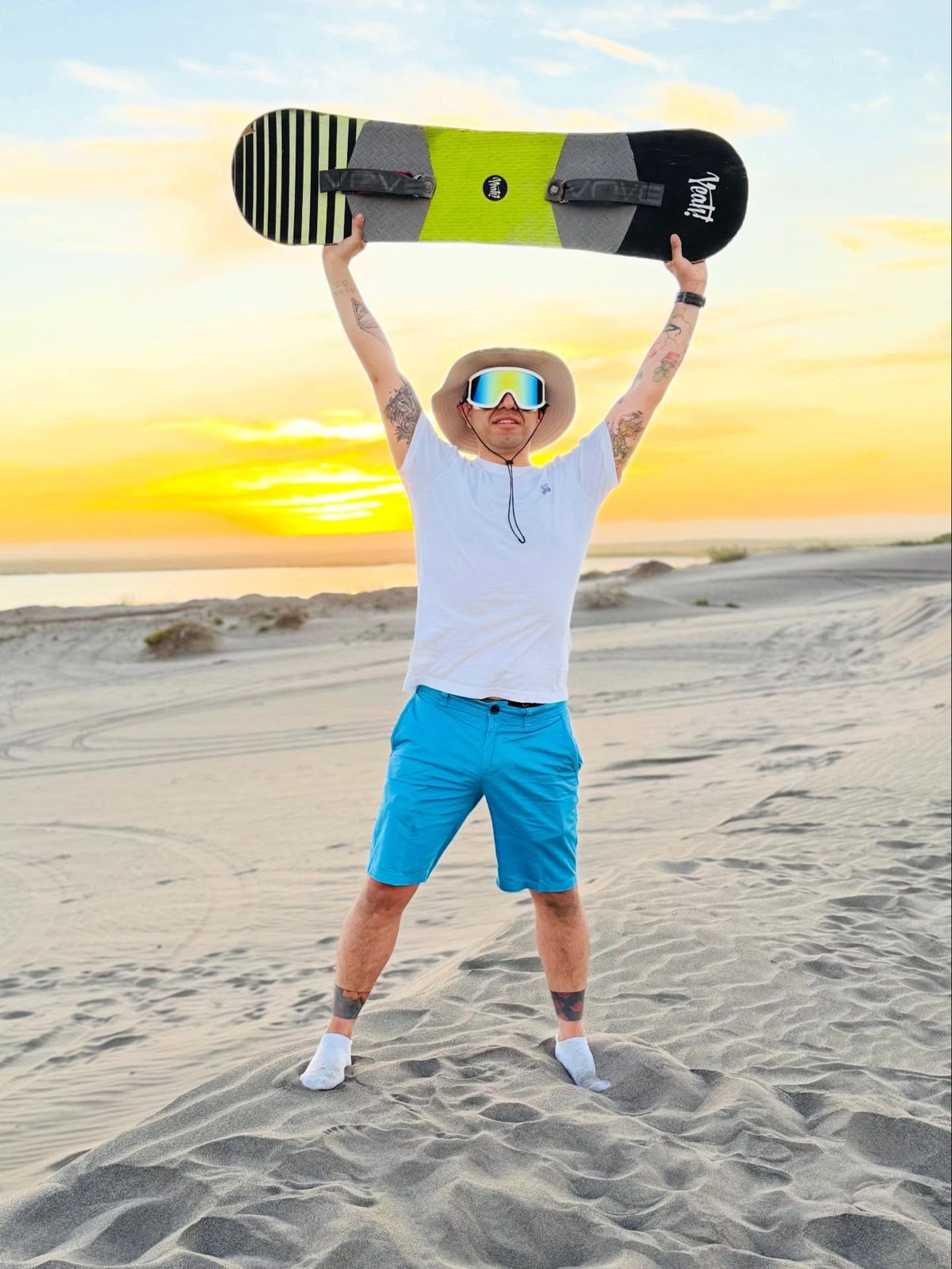 Cliente levantando la tabla de sandboard sobre las dunas al atardecer